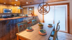 A kitchen with wooden cabinets, a stainless steel microwave, and a wooden dining table with chairs.