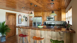 A kitchen with wooden cabinets, a stainless steel refrigerator, and a wooden bar counter with stools.