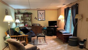 A cozy living room with a sofa, armchair, and a television. There is a bookshelf with various items and a decorative wall piece. - Minutes from Everything- Lambeau Field,  Door County and more !, (Hobart)