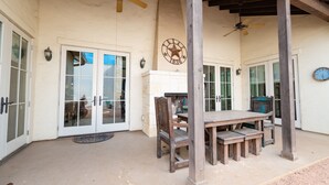 A covered patio with a wooden table and chairs, a ceiling fan, and a clock on the wall.