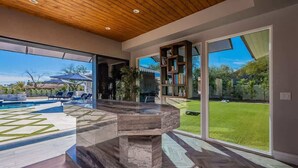 Un intérieur moderne avec une grande porte vitrée donnant sur un jardin, une cheminée en pierre et une bibliothèque.