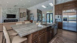Une cuisine moderne dotée d’un îlot en marbre, d’appareils électroménagers en acier inoxydable et d’un coin salon confortable avec un téléviseur.