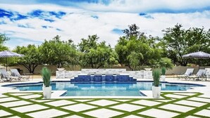 Une piscine dont le fond est décoré de motifs géométriques en mosaïque, entourée de chaises longues et de parasols.