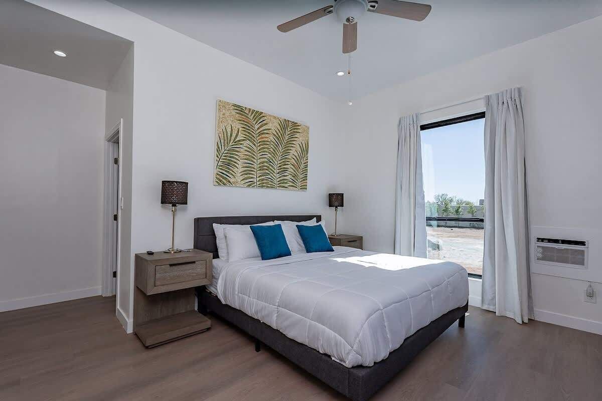 A modern bedroom with a large bed, two bedside tables, a ceiling fan, and a window with curtains.