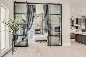 A modern interior with a sliding glass door leading to a bedroom, a fireplace, and a kitchen area.