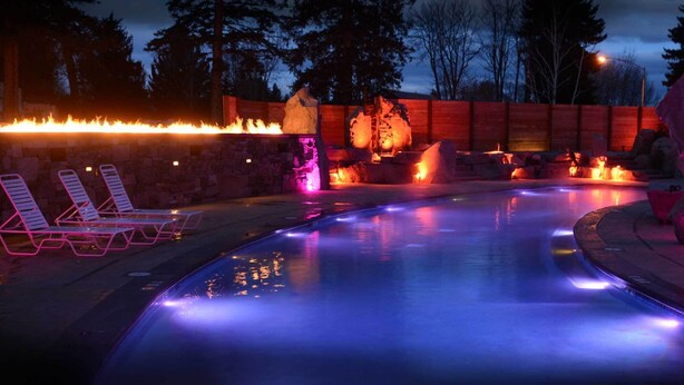 A heated outdoor pool area with lounge chairs and a fire feature.