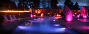 A heated outdoor pool area with lounge chairs and a fire feature.