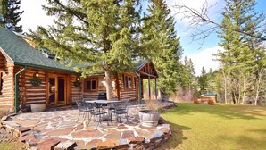 A log cabin with a stone patio, outdoor seating, and a fire pit.