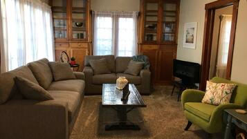 Een woonkamer met twee banken, een salontafel, een groene fauteuil en houten kasten.