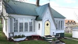 A white house with a green roof, a yellow front door, and a small porch with potted plants.