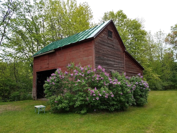 A wooden barn with a green roof, surrounded by lush greenery and blooming flowers.