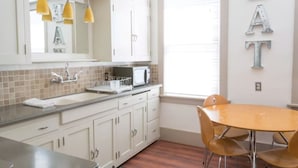 A kitchen with white cabinets, a microwave, and a sink. There is a window with blinds and a table with chairs.