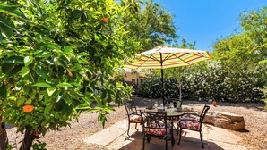 An outdoor patio with a table and chairs, surrounded by greenery and a large umbrella. - “La Casita Encantada” All the Charm & all the Amenties for a Long or Short Stay! (Tucson)