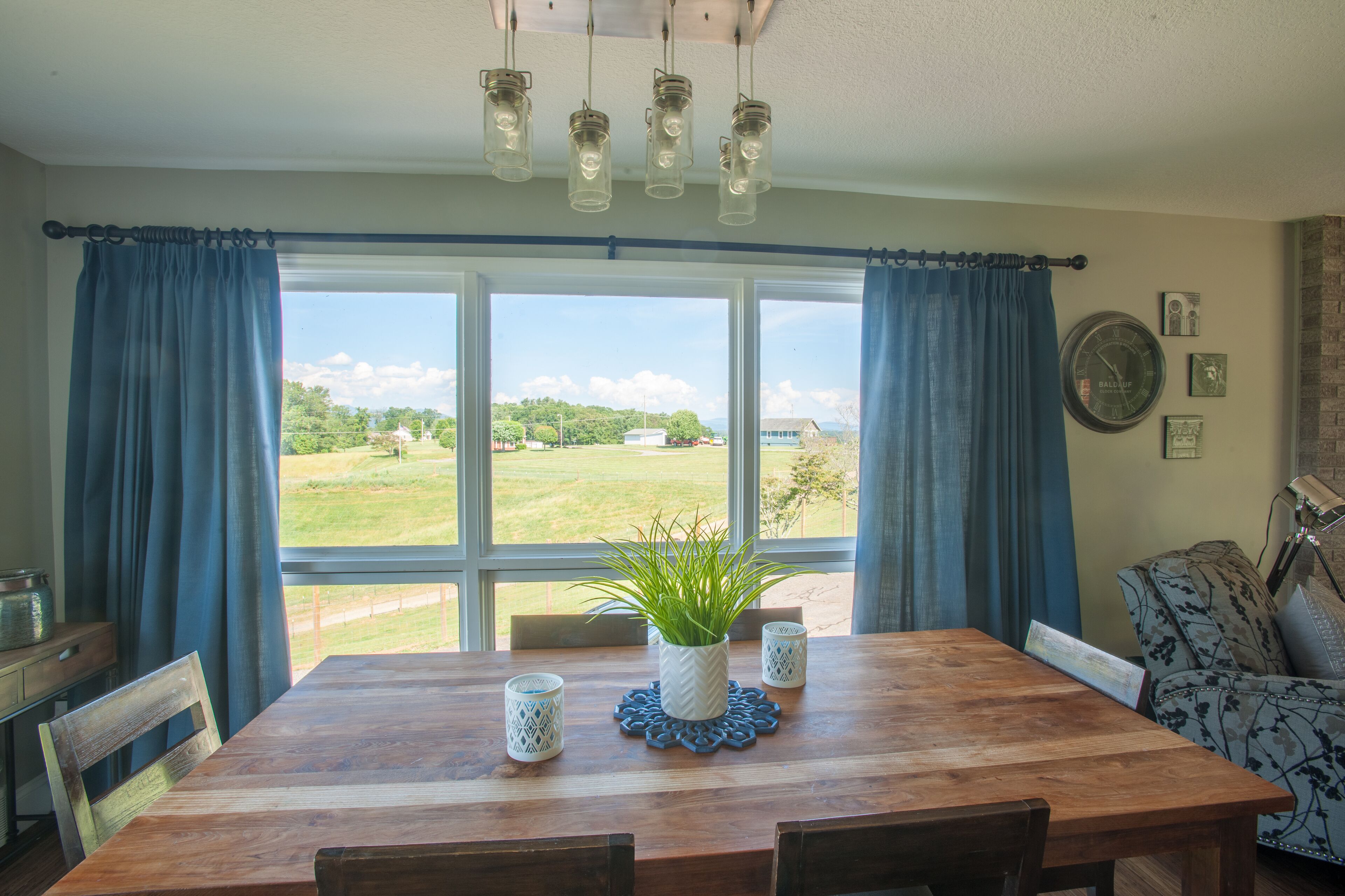 Un coin repas avec une table en bois, des rideaux bleus et une vue sur un paysage verdoyant.