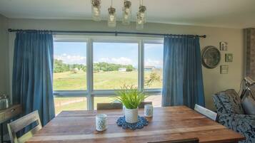 Un coin repas avec une table en bois, des rideaux bleus et une vue sur un paysage verdoyant.