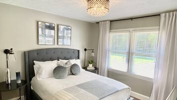 Une chambre à coucher avec un grand lit, des tables de chevet, un lustre et une fenêtre avec des rideaux.