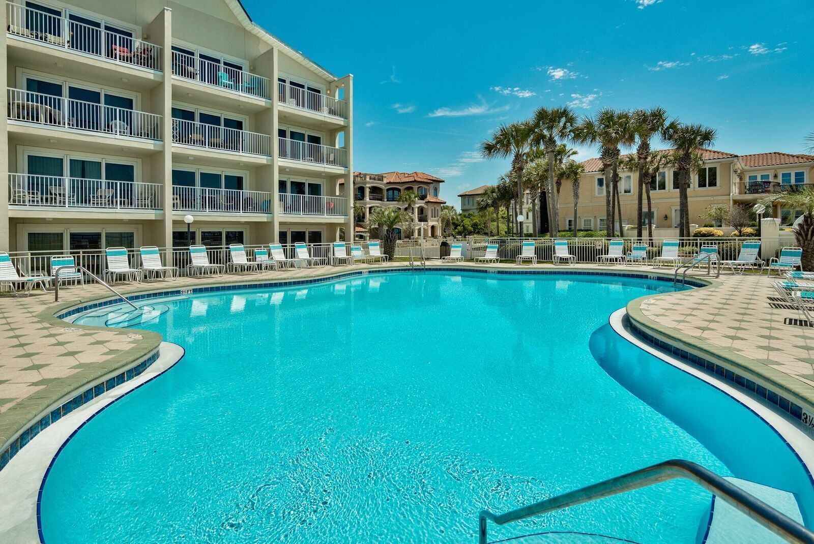 A swimming pool with lounge chairs and a multi-story building with balconies.