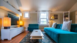 En moderne stue med et fladskærms-tv, et hvidt sofabord, teal farvede sofaer og en gulvtæppe med et mønster.