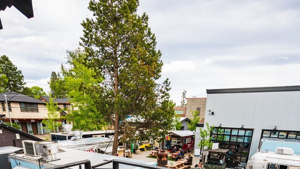 En træterrasse med grill og siddeplads, med udsigt over en parkeringsplads med autocampere og en bygning med store vinduer.