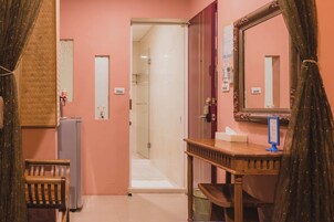 A hotel room with a wooden vanity, a mirror, a door leading to a bathroom, and a small table with a tissue box.