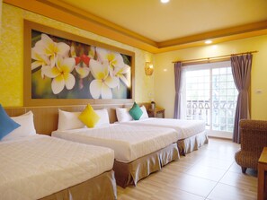 Een hotelkamer met twee bedden, een groot bloemen schilderij aan de muur, een raam met gordijnen, en een rieten stoel.