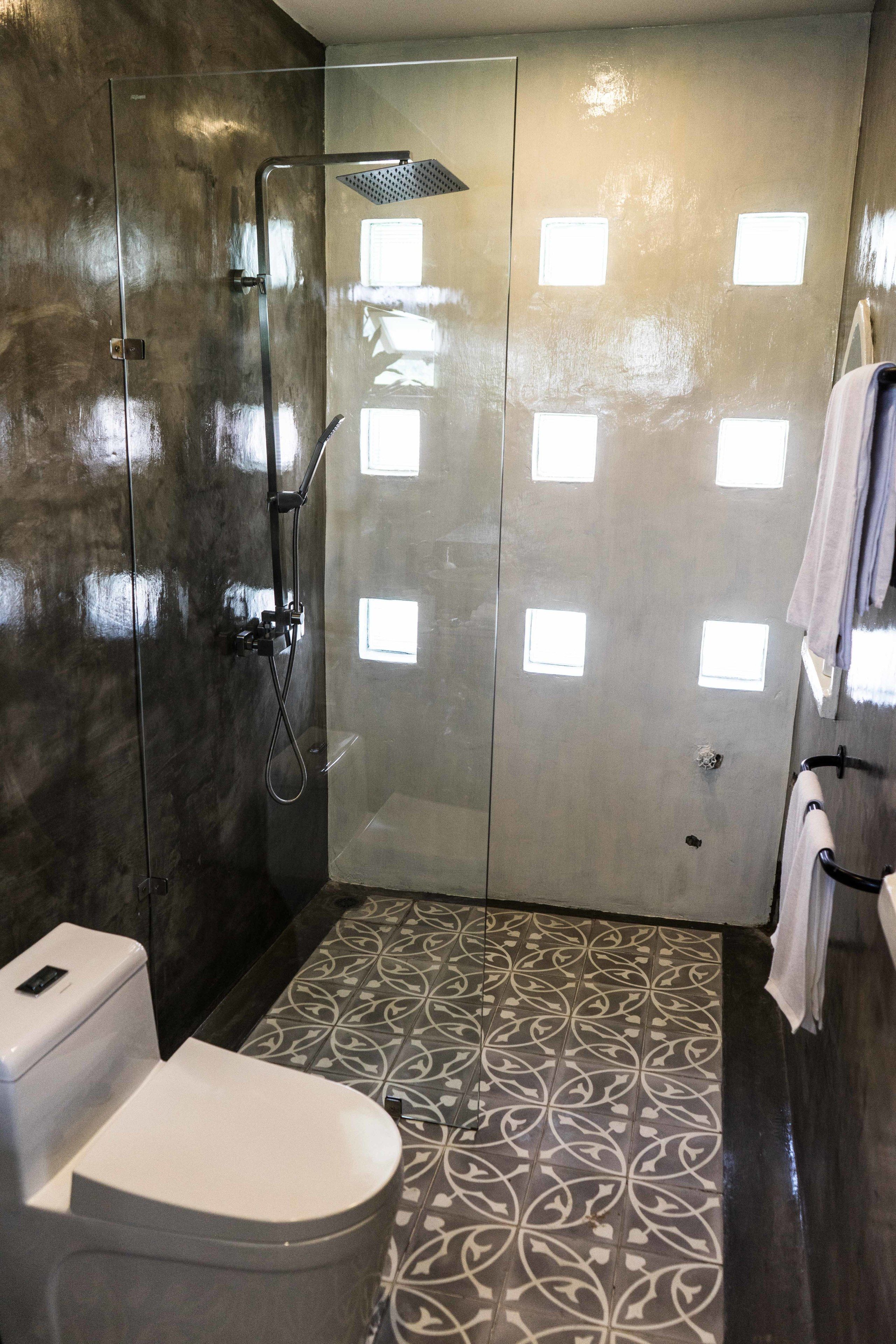 Ein modernes Badezimmer mit einer Duschkabine aus Glas, einer Toilette und gefliestem Boden mit Muster.