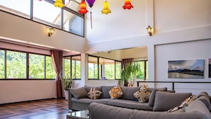 Uma sala de estar espaçosa com sofá cinzento, janelas amplas e vista para o verde.