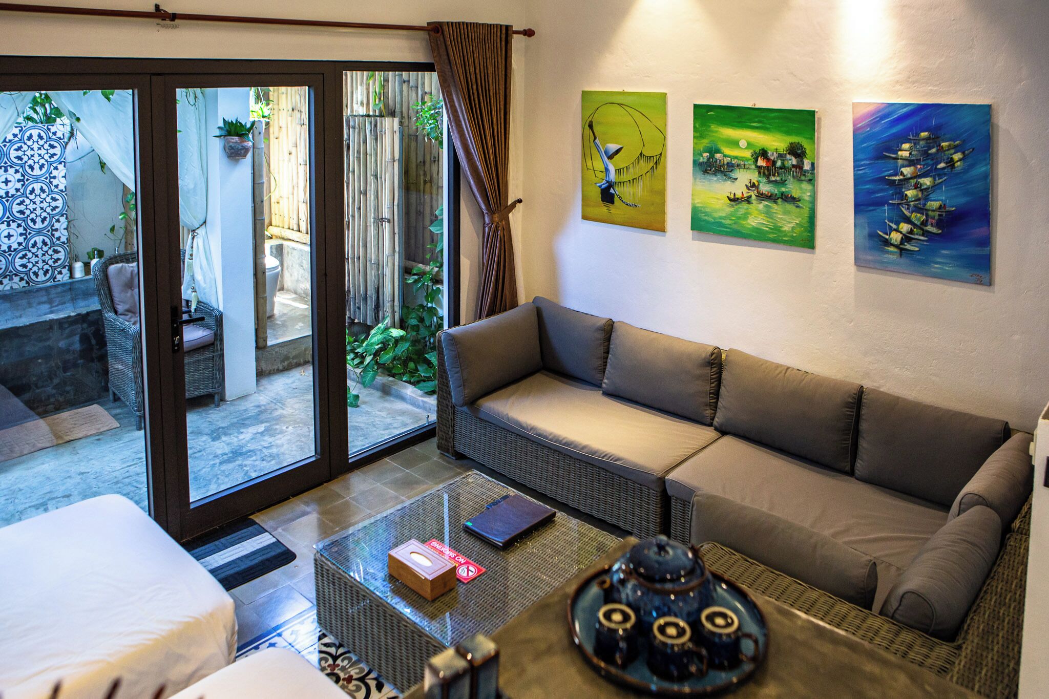 Una habitación con sofá, una mesita de centro de vidrio y vistas a un espacio exterior con valla de bambú y plantas.
