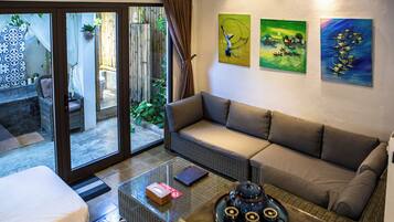 Een kamer met een bank, een glazen salontafel en uitzicht op een buitenruimte met een bamboomschutting en planten.