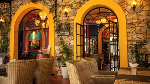 Restaurante com mobiliário de vime, paredes de pedra e lanternas penduradas.
