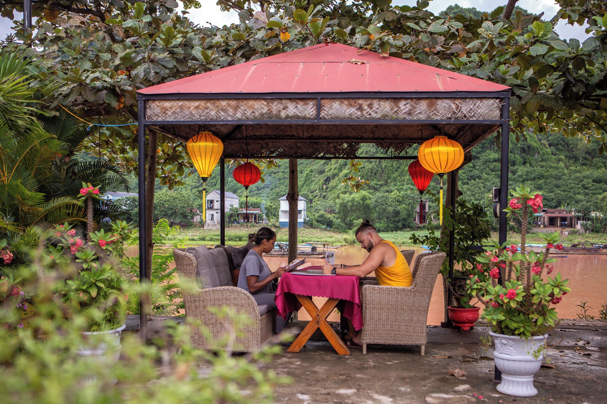 Un pabellón con techo rojo, muebles de mimbre y plantas en macetas.