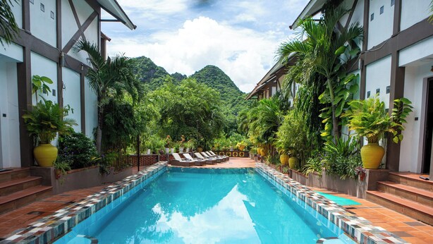 Uma piscina retangular com borda em azulejos, rodeada por vegetação exuberante e um cenário montanhoso.