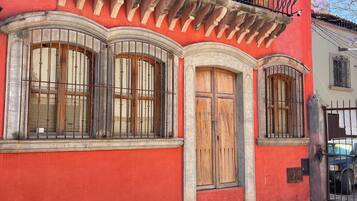Un edificio rojo con balcón, ventanas grandes y puerta de madera.