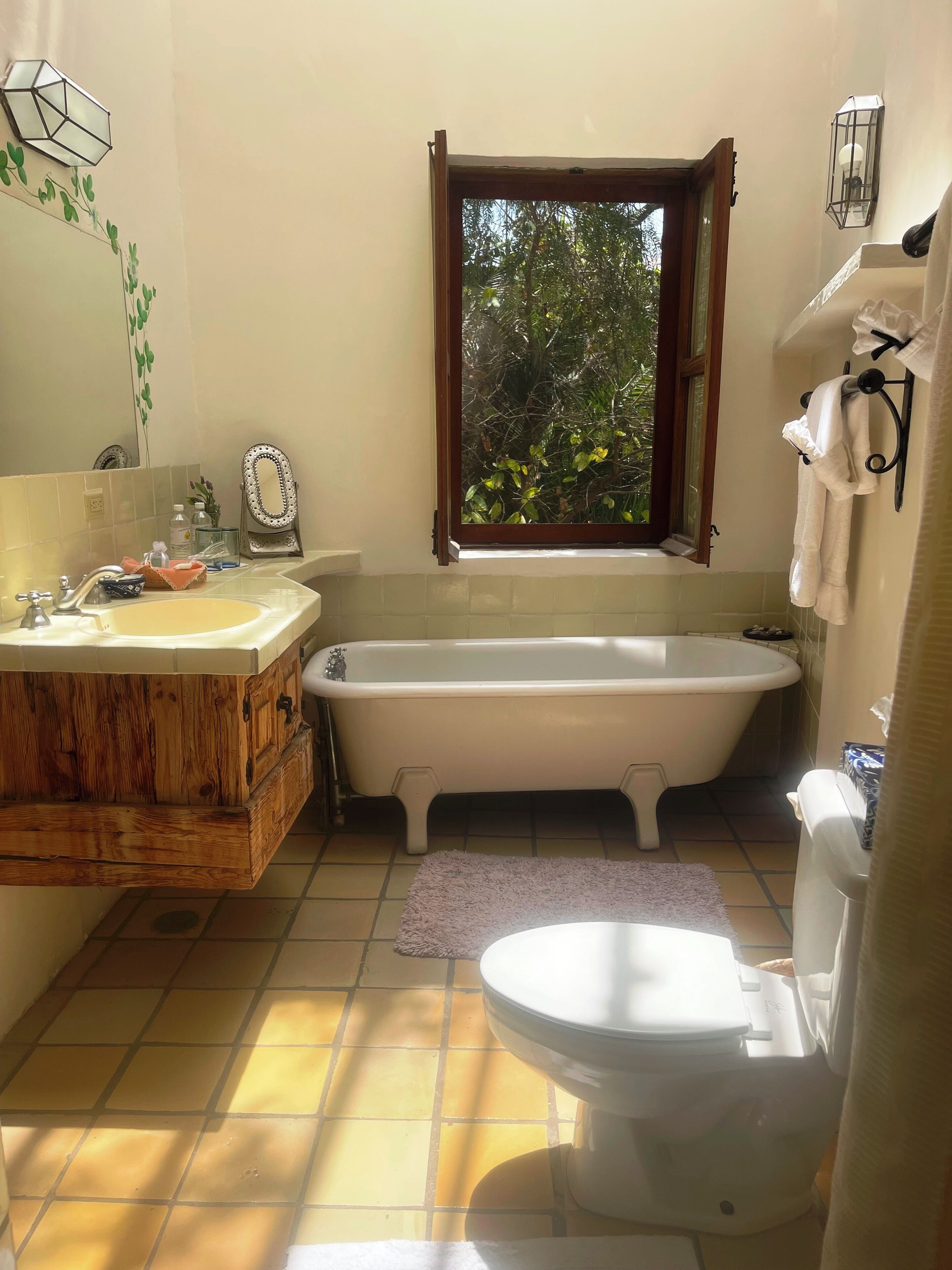 Un baño con tocador de madera, bañera, inodoro y ventana con vista a la vegetación.