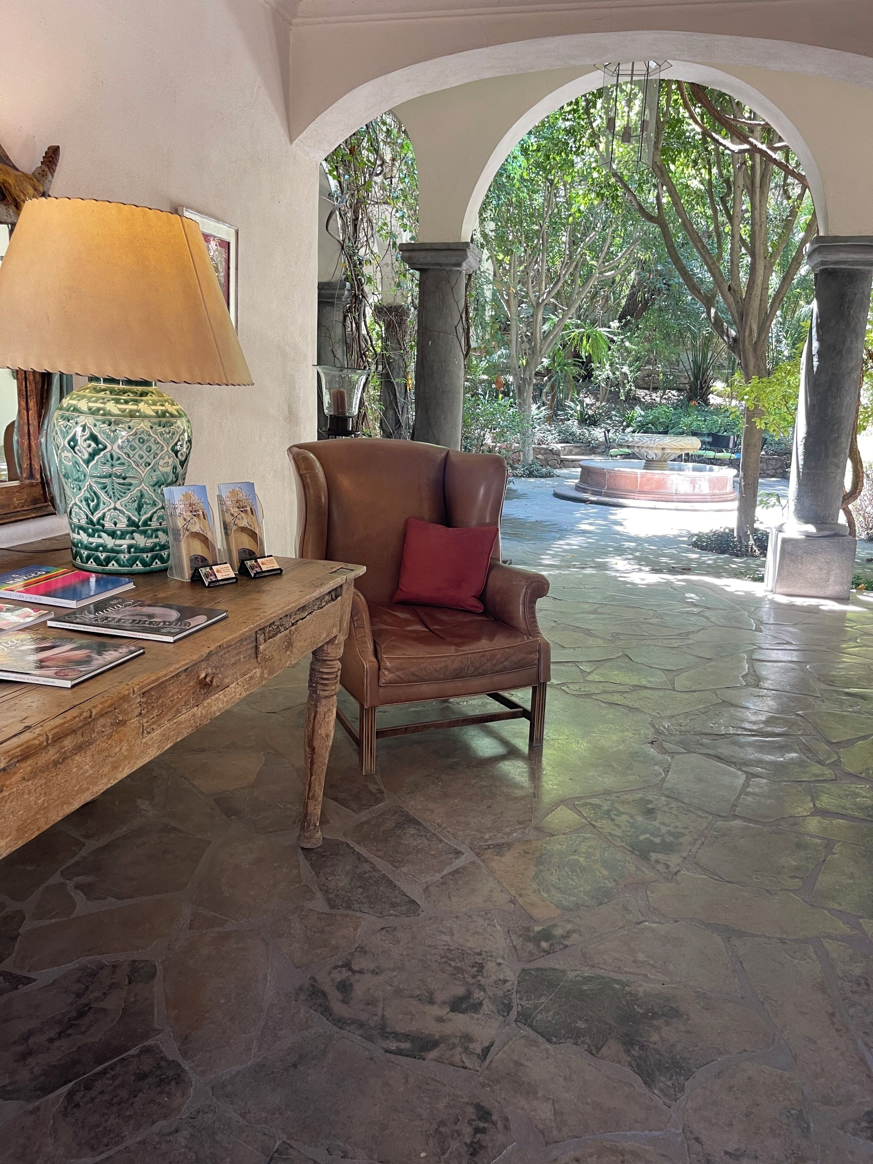 Un vestíbulo con suelo de piedra, un sillón de cuero y una mesa con libros y una lámpara.