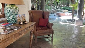 Un vestíbulo con suelo de piedra, un sillón de cuero y una mesa con libros y una lámpara.