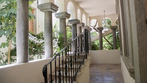 Escadaria coberta ao ar livre, com colunas de pedra e corrimão de metal, cercada por vegetação.
