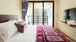 A bedroom with a bed, a TV, and a balcony with a view of greenery. - Haku Beach Days Inn (Hengchun)