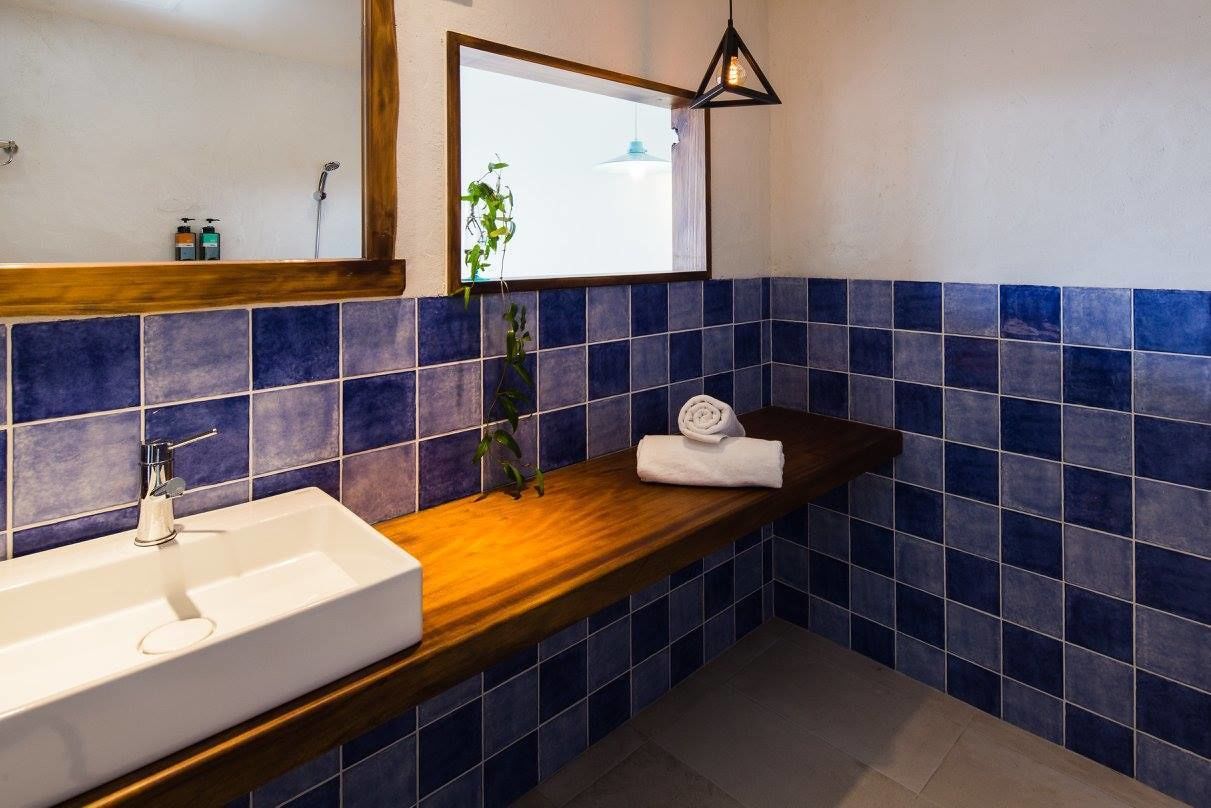 A bathroom with a white sink, a wooden countertop, a mirror, and blue-tiled walls.