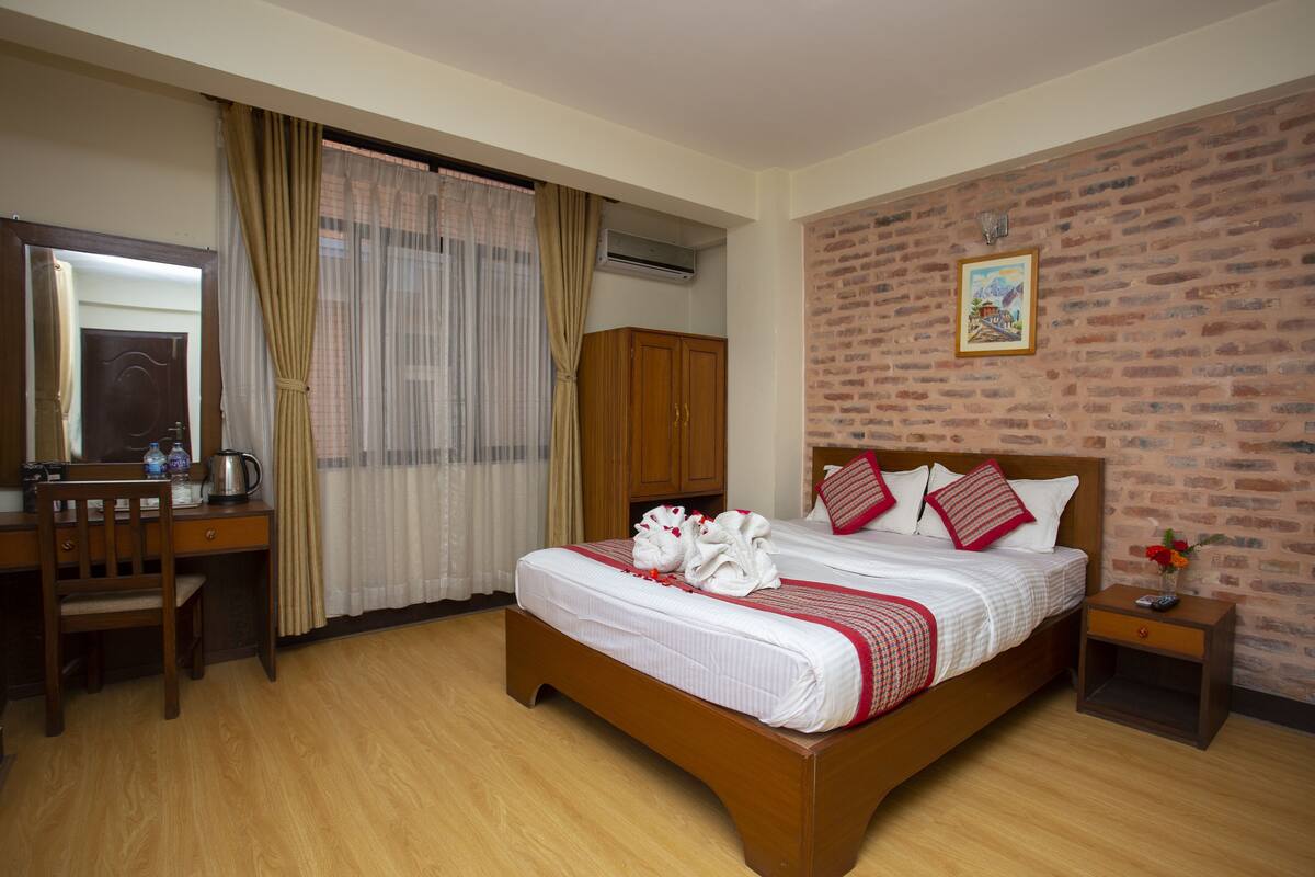 Una habitación de hotel con una cama de madera, un escritorio con una silla, una mesita de noche y una pared de ladrillo.