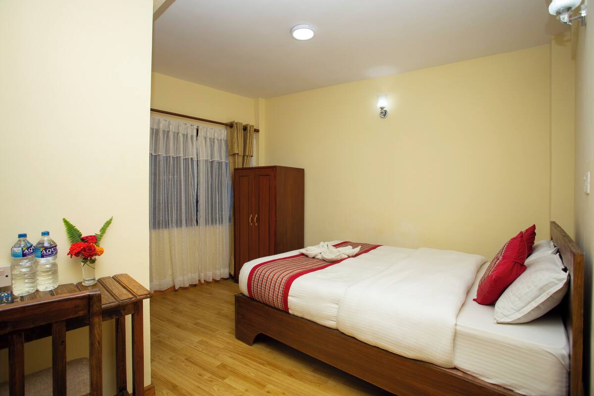 Habitación de hotel con cama, muebles de madera, un escritorio con botellas de agua y un jarrón con flores.