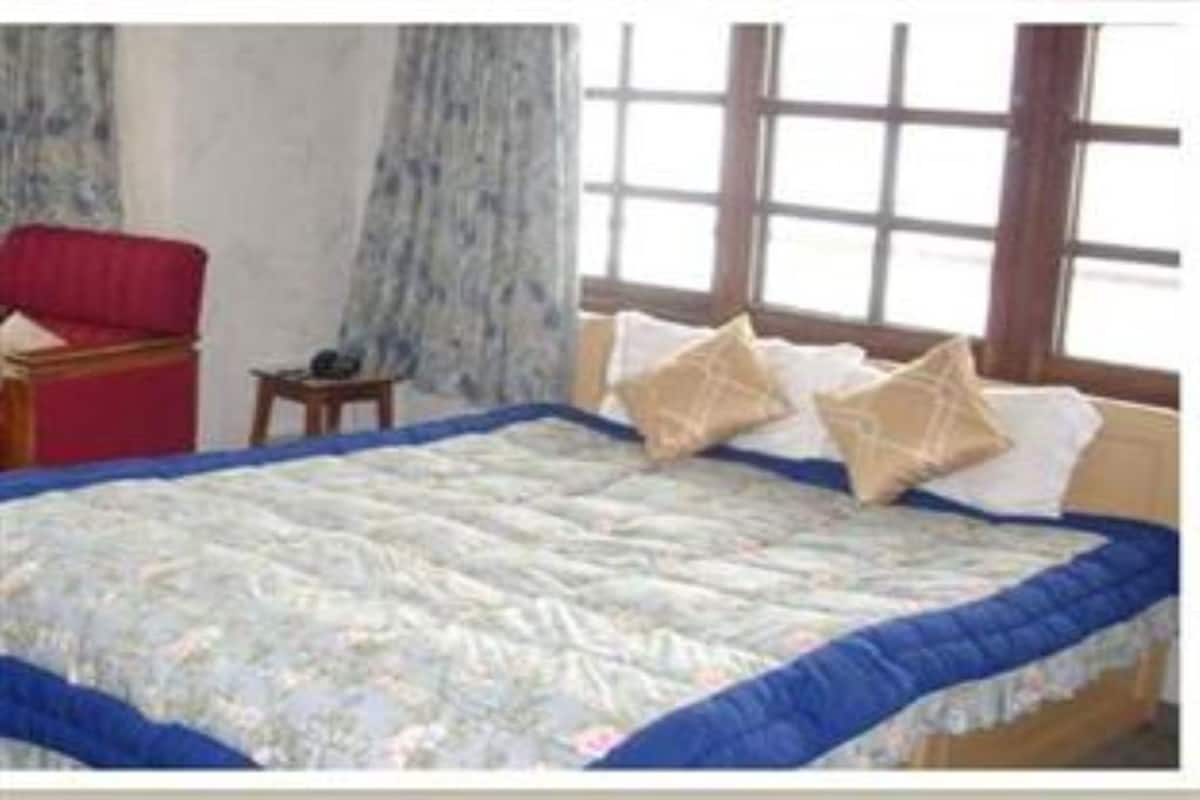 Une chambre à coucher avec un grand lit, un fauteuil rouge, une petite table et une fenêtre avec des rideaux.