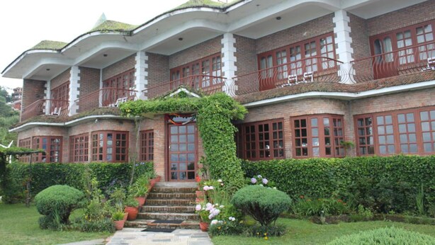 A large, multi-story building with a brick facade, large windows, and a central entrance with steps. - Niva Niwa Lodge (Baluwapati Deupur)