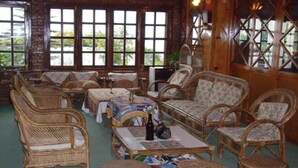A room with wicker furniture, large windows, and a view of greenery outside. - Niva Niwa Lodge (Baluwapati Deupur)