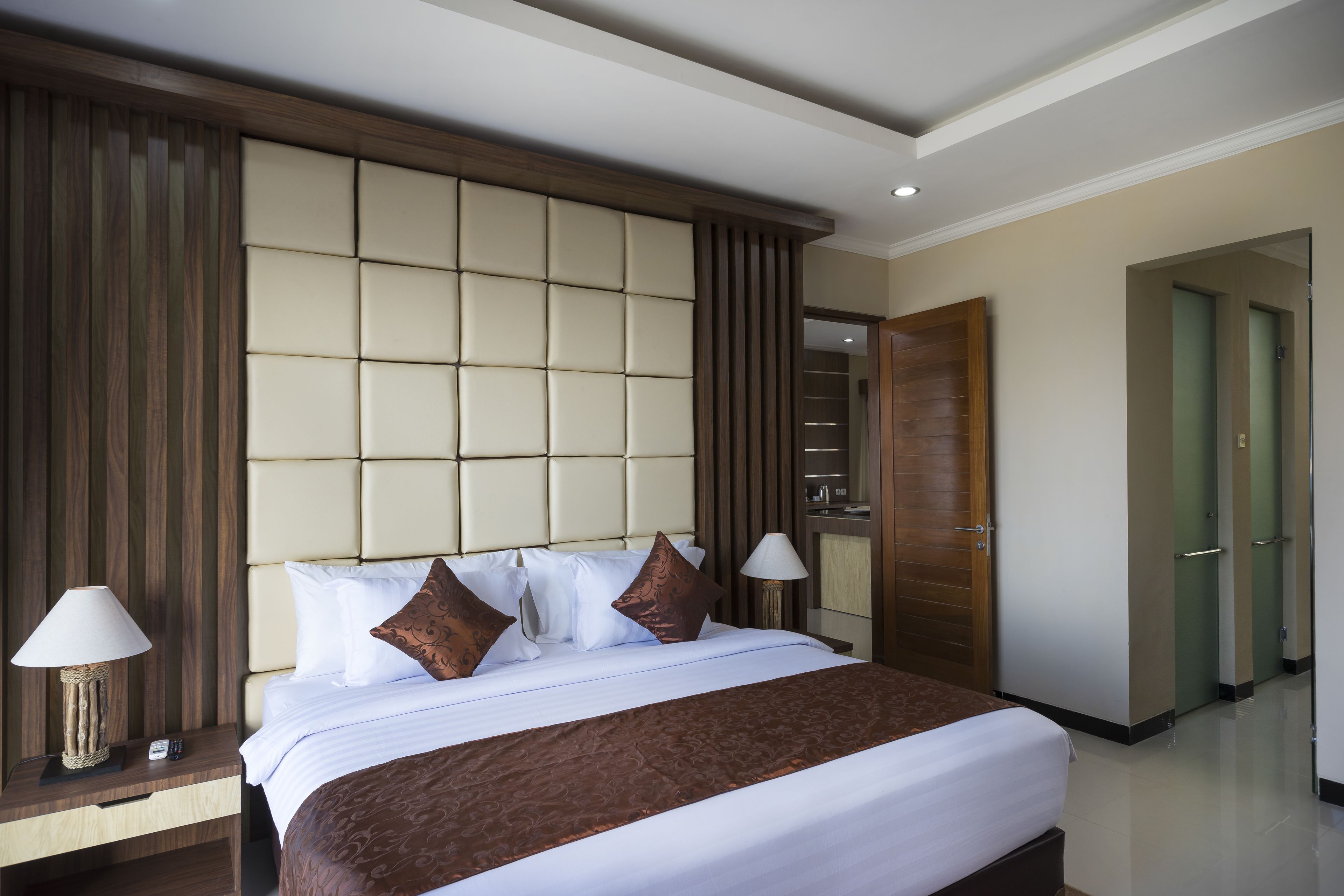 A hotel room with a large bed, a wooden headboard, a nightstand with a lamp, and a wardrobe.