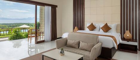 A bedroom with a large bed, a sofa, a coffee table, and a view of the outdoors.