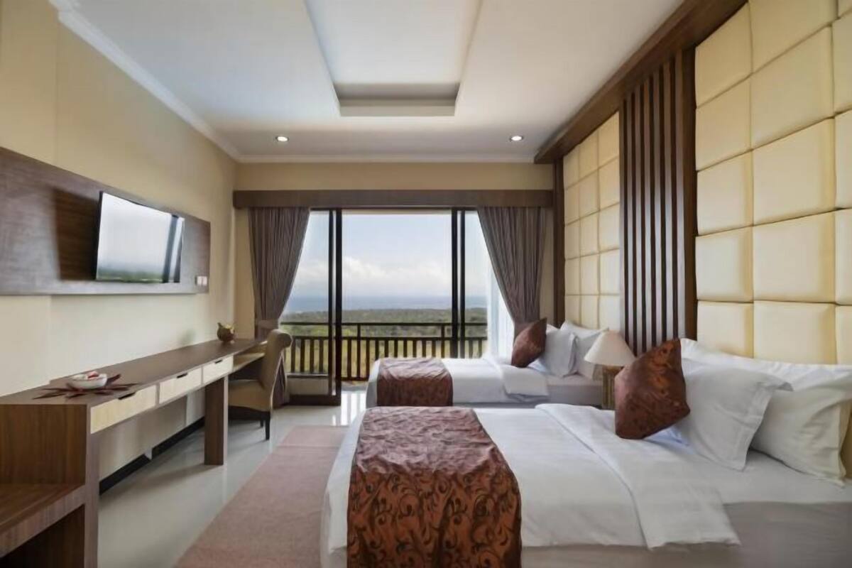 Habitación de hotel con cama, escritorio, silla, televisor y balcón con vistas.