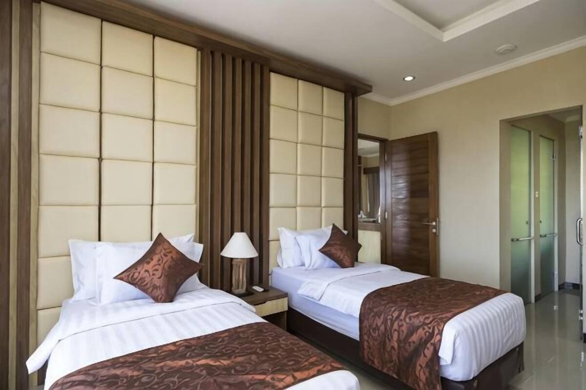 Una habitación de hotel con dos camas, un cabecero de madera, una mesita de noche y un espejo.