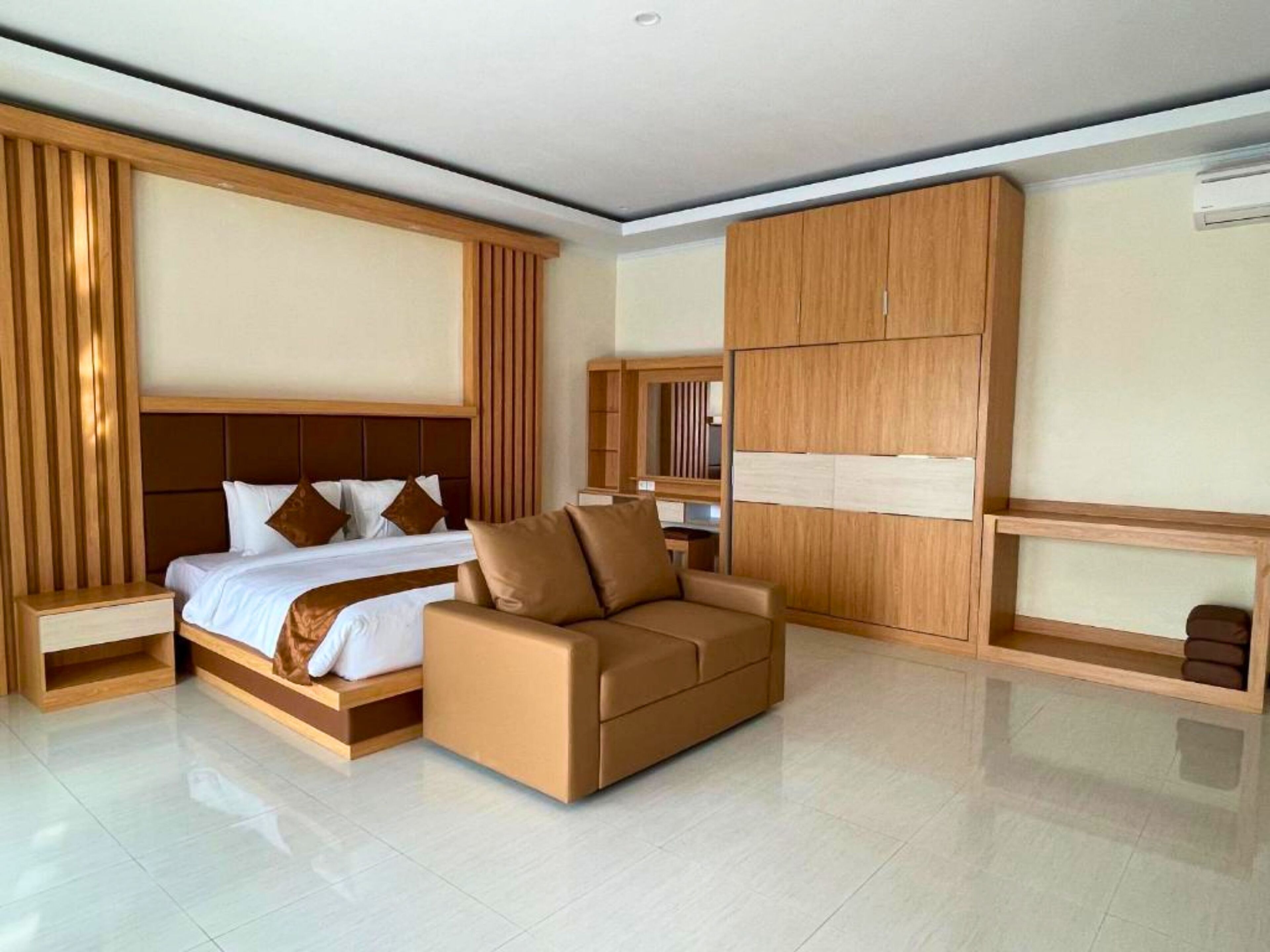 A modern hotel room with a large bed, a sofa, a wardrobe, and a mirror.