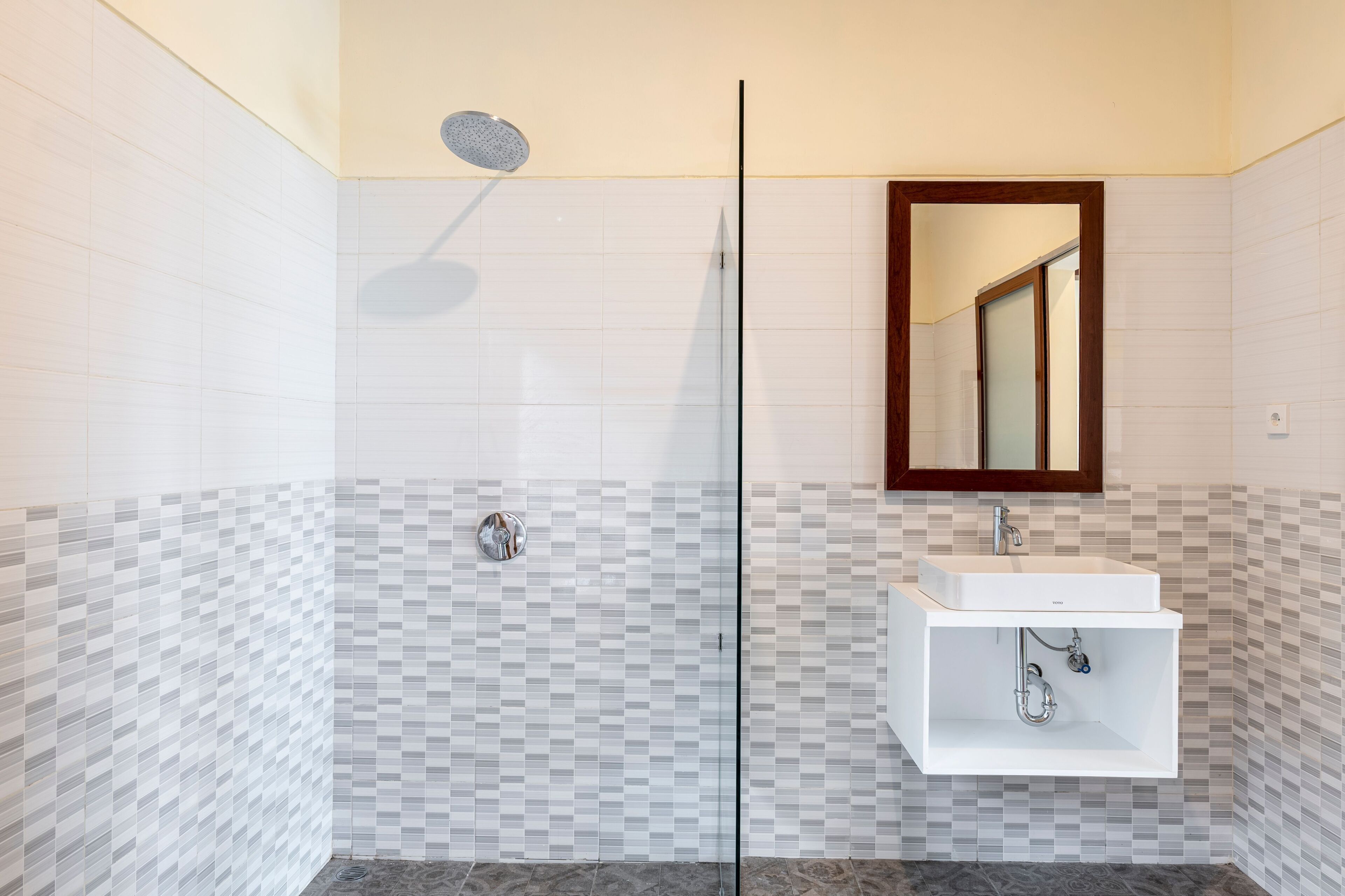 A modern bathroom with a glass shower enclosure, a white sink with a mirror above it, and a tiled floor.